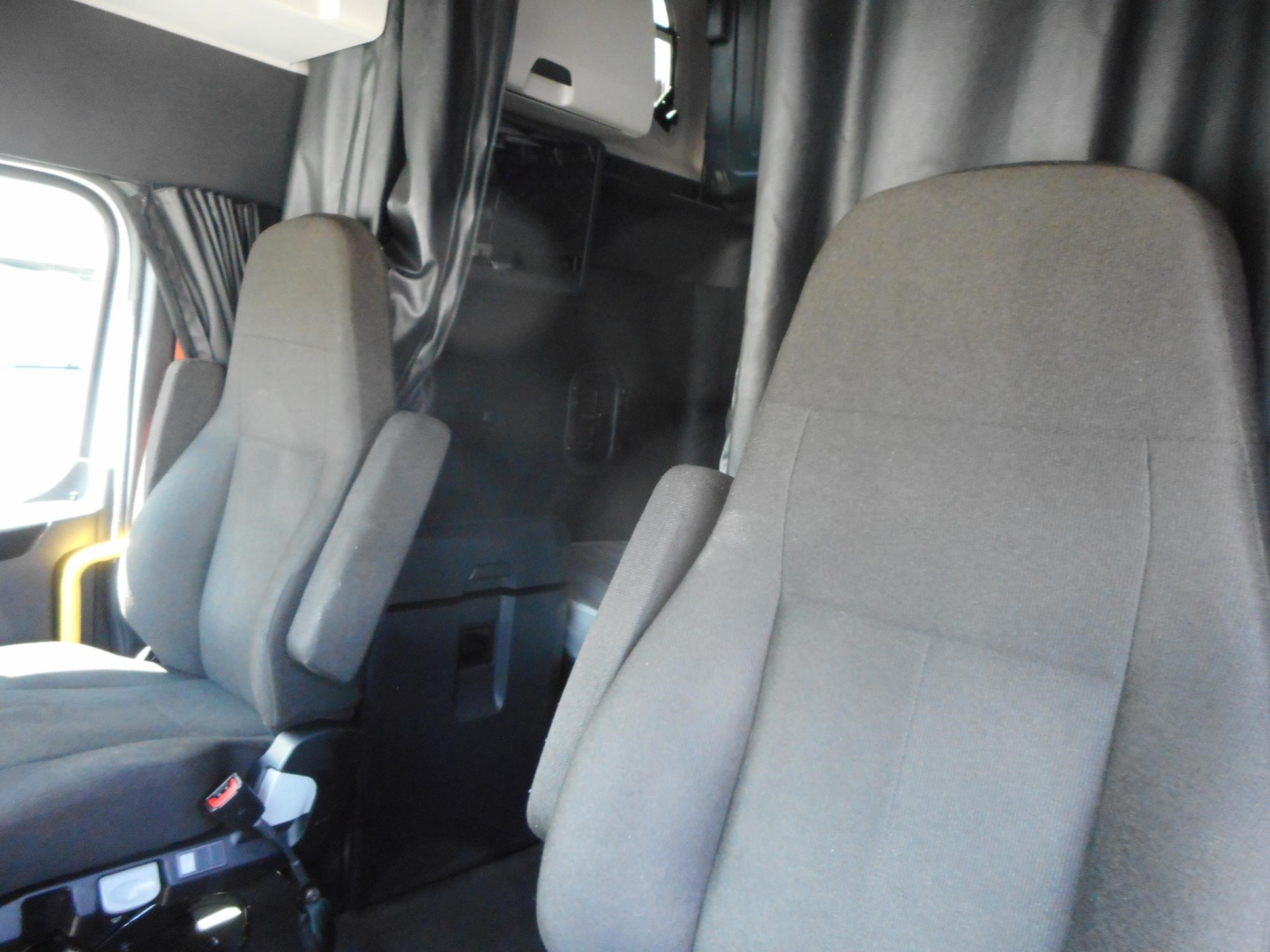 Cab interior of a Freightliner truck showing two front seats and partition; dashboard area visible with curtains and sleeper area in background.