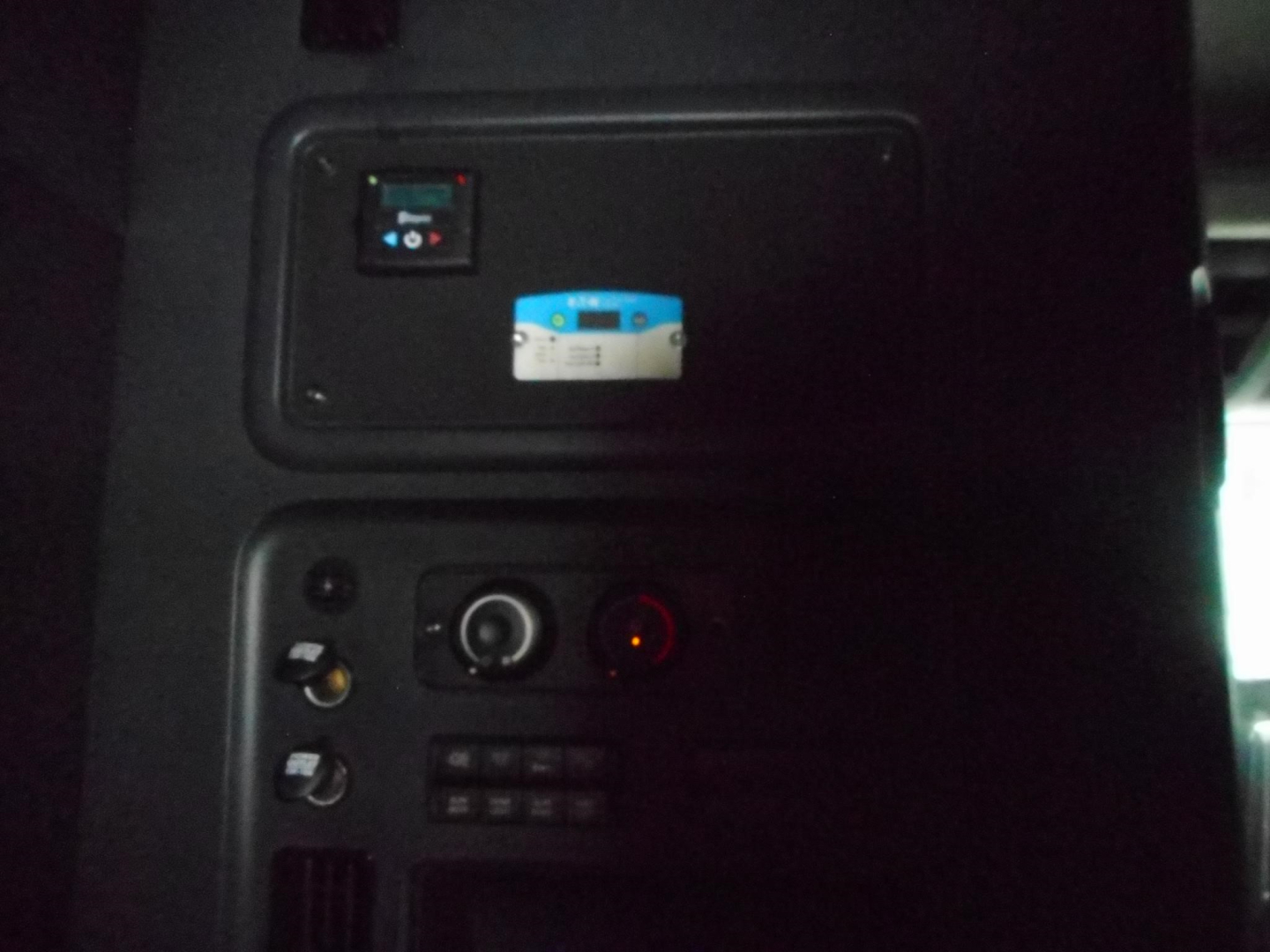 Truck cab interior panel with switches and a small blue-and-white label; dashboard area showing a control panel and round indicator light.