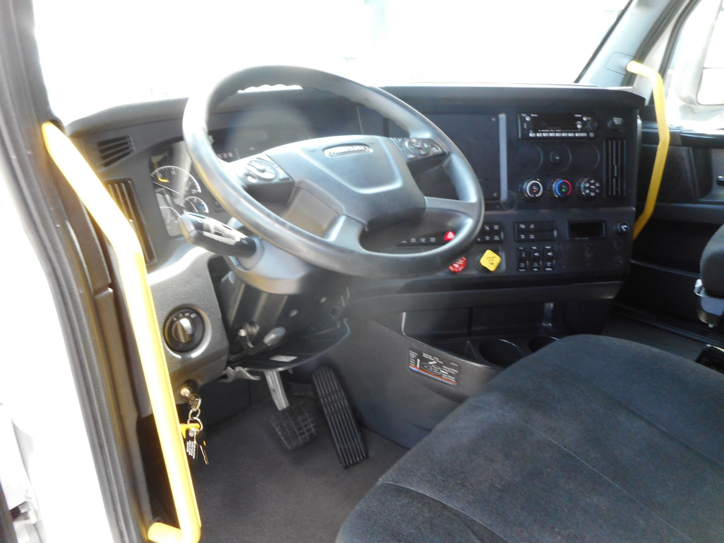 Truck cab interior showing steering wheel, instrument cluster, and dashboard of a Freightliner Cascadia 126 day cab with driver seat and pedals visible.