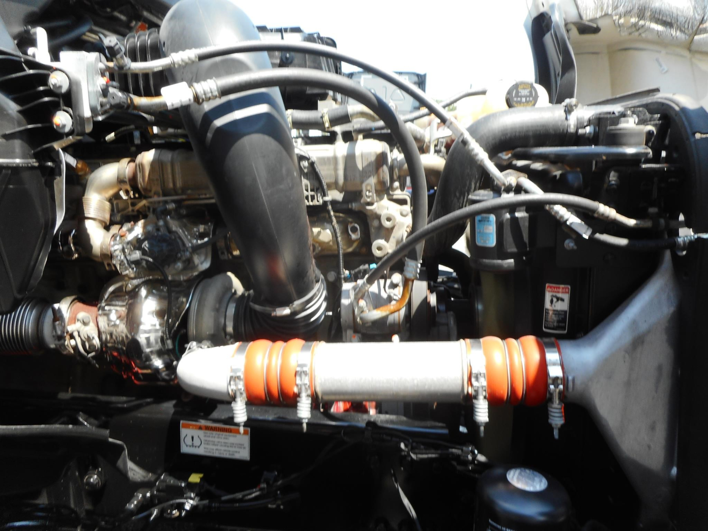 Freightliner Cascadia engine bay showing intake hoses, turbocharger, intercooler piping, orange flexible couplings, and various hydraulic lines.