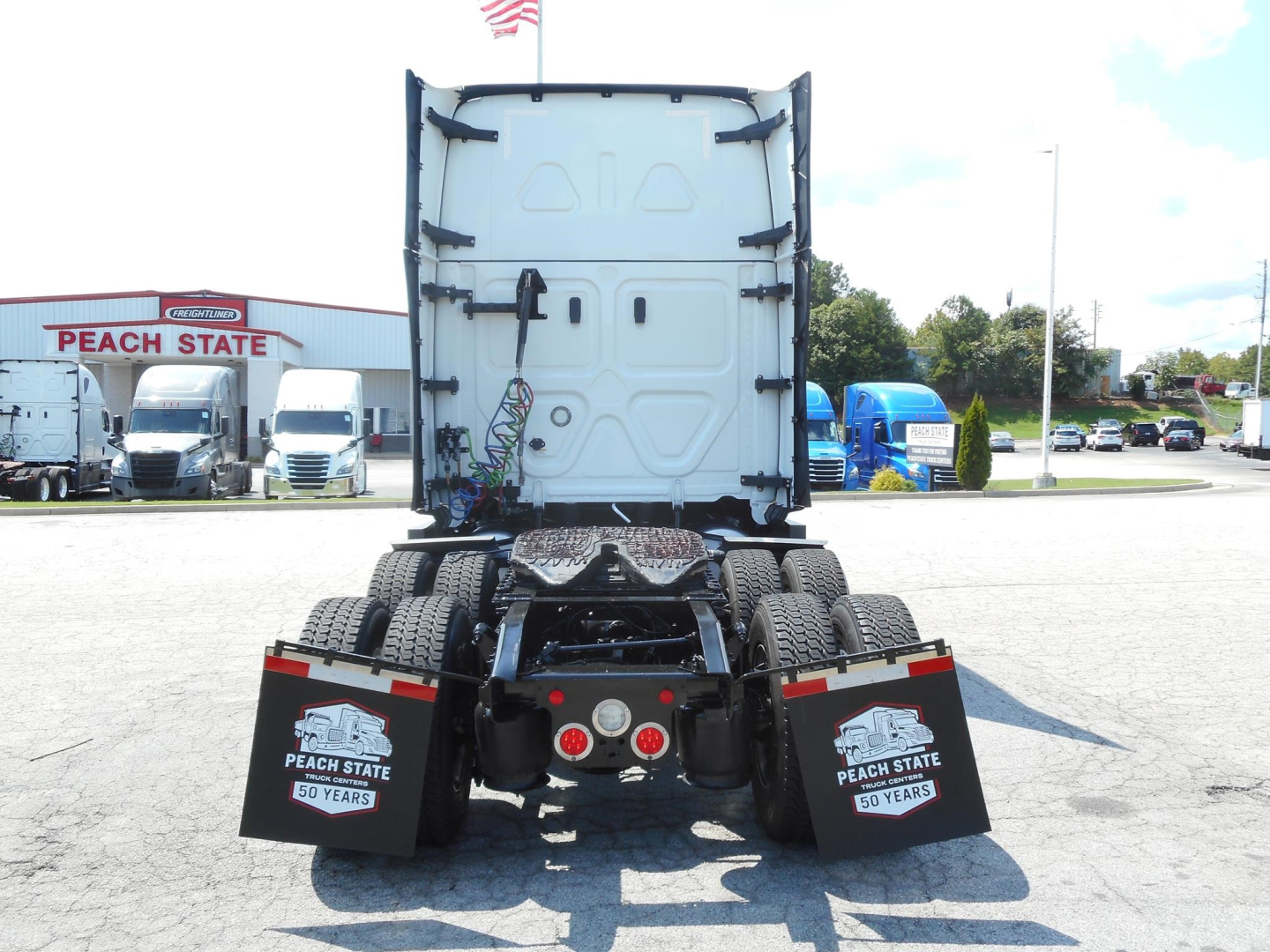 Rear view of a Freightliner Cascadia truck tractor chassis showing fifth wheel and dual rear axles, mud flaps with Peach State 50 years insignia, and fifth-wheel connectors.
