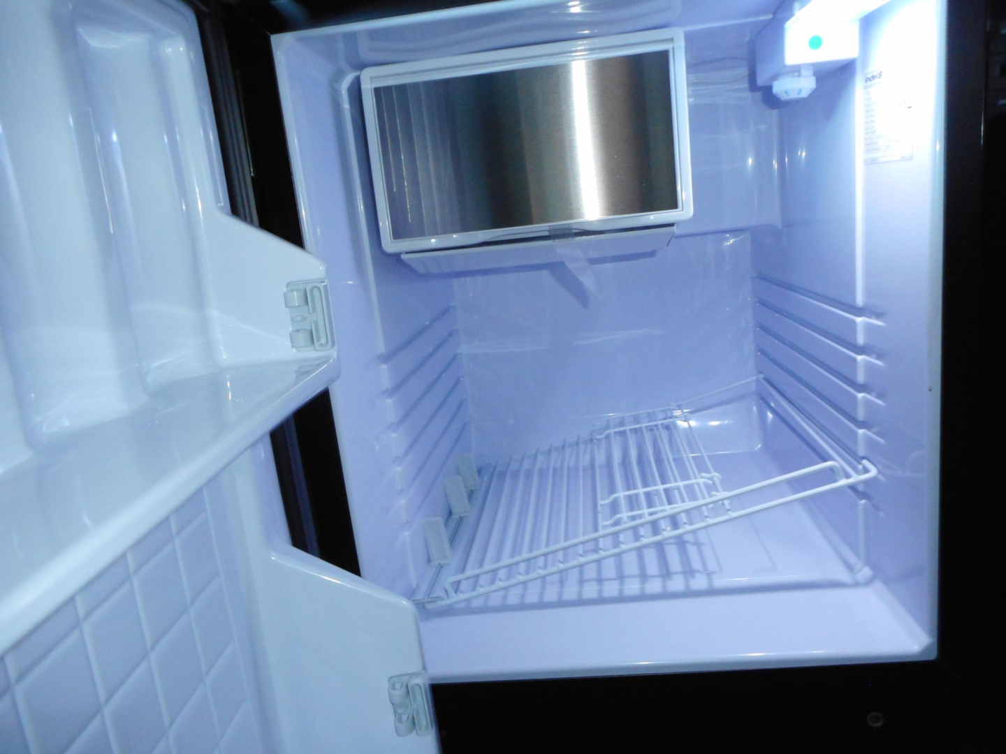 Freightliner Cascadia truck cab interior showing empty sleeper fridge area with open door and light, compact refrigerator/freezer unit mounted on wall.