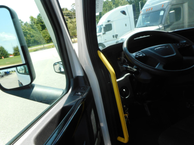 Cab interior of a 2024 Freightliner Cascadia 126 truck showing steering wheel, dashboard, and doorway with yellow grab handle.