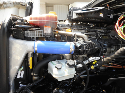 Freightliner Cascadia 126 engine bay showing coolant reservoir, blue silicone intercooler hose, brake reservoir, and various engine components.