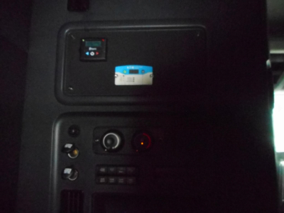 Truck cab interior panel with switches and a small blue-and-white label; dashboard area showing a control panel and round indicator light.