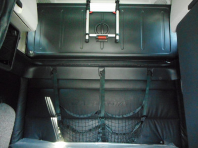 Truck sleeper cab storage area with a fitted strap and net pocket, view showing back of sleeper and a metal panel or trunk area