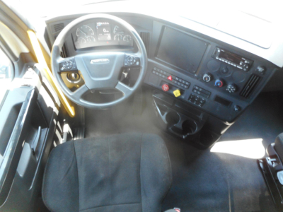 Truck cab interior showing steering wheel, dashboard with digital display, center console with climate controls, and two cup holders.