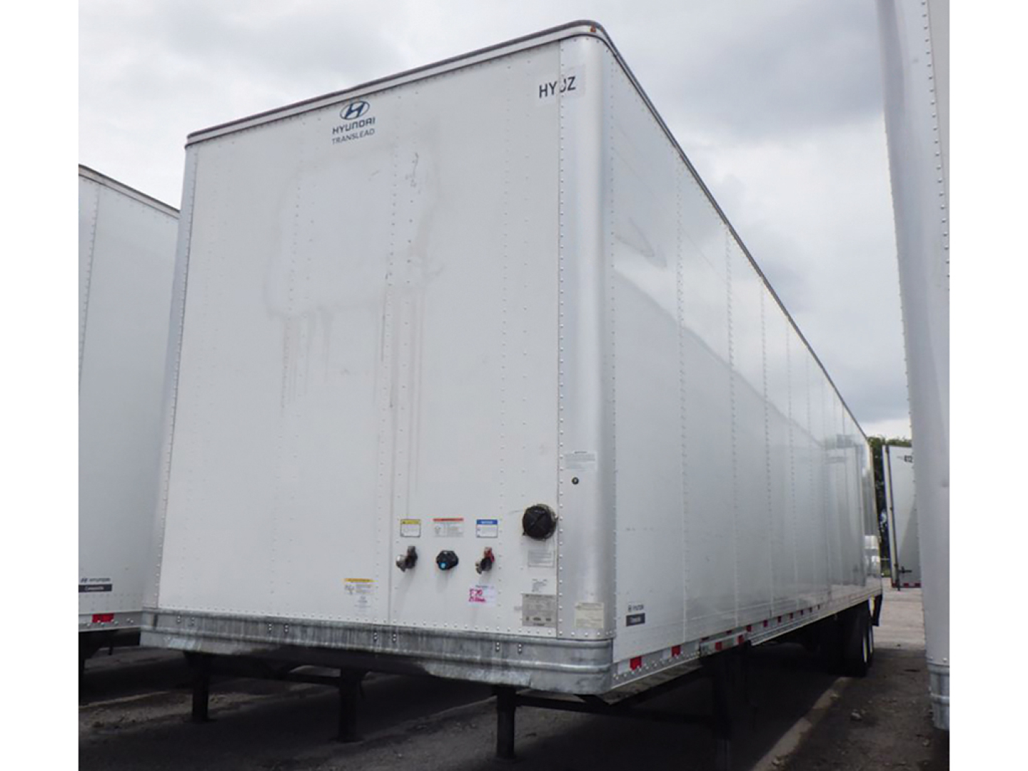 Hyundai HYZ cargo van trailer with a tall rectangular white exterior and rear doors; small control valves and labels near lower rear corner.