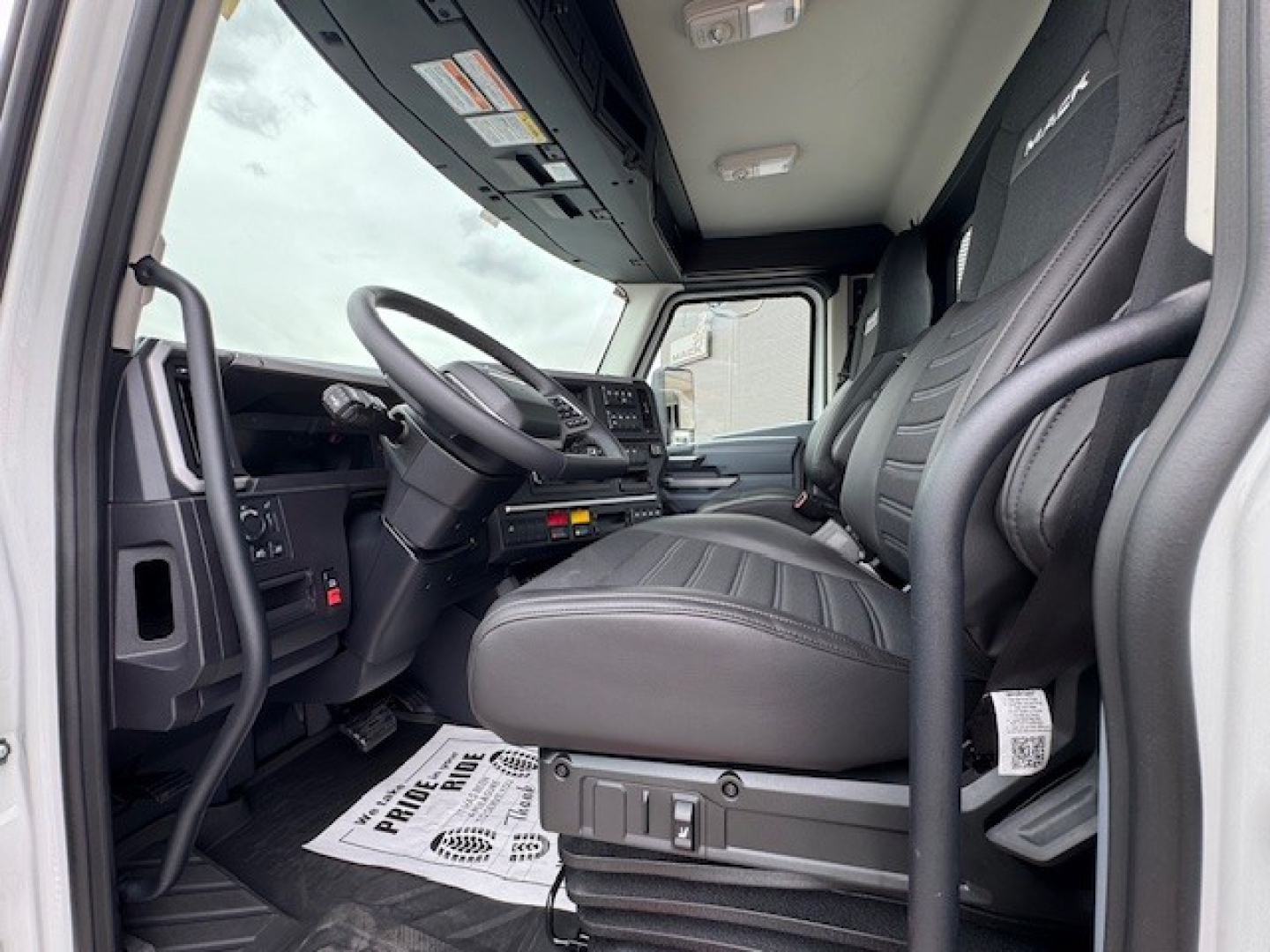 Cab interior of a new Mack AN64T daycab truck showing driver seat, steering wheel, dashboard, and front passenger seat.