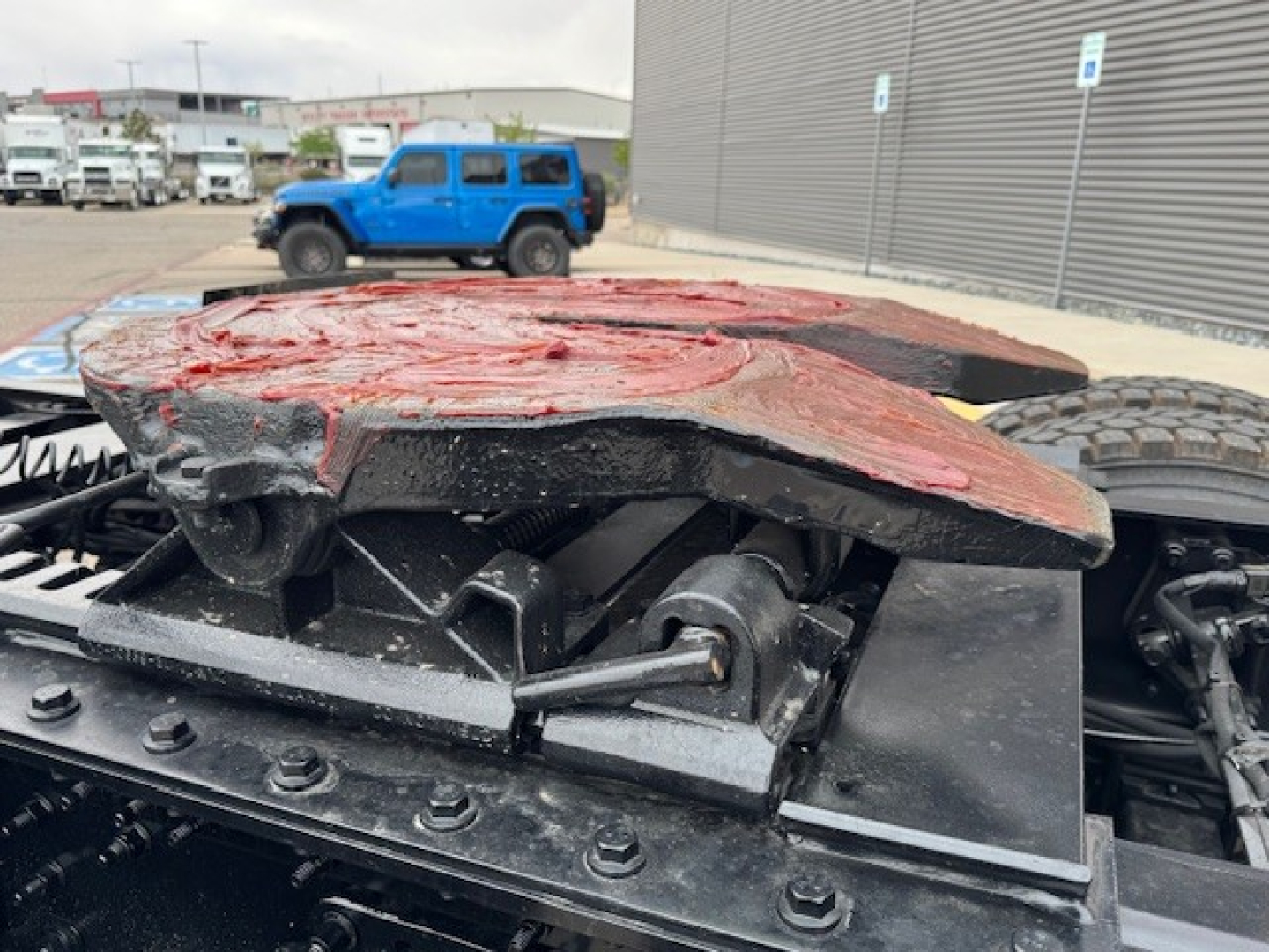 View of a Mack AN64T truck chassis with a damaged red cab fairing resting on a black framework; visible components include hinge mechanisms, bolts, and support plate.