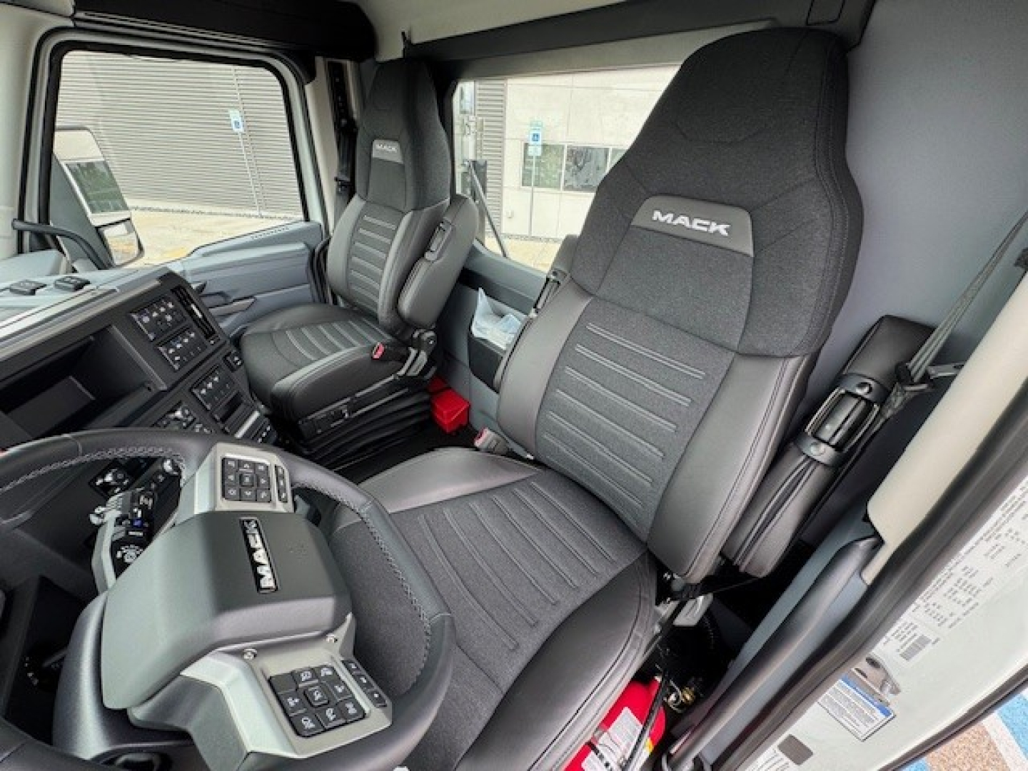 Interior of a new Mack AN64T daycab showing driver and passenger seats with Mack logo, dashboard controls, steering wheel, and seating area.