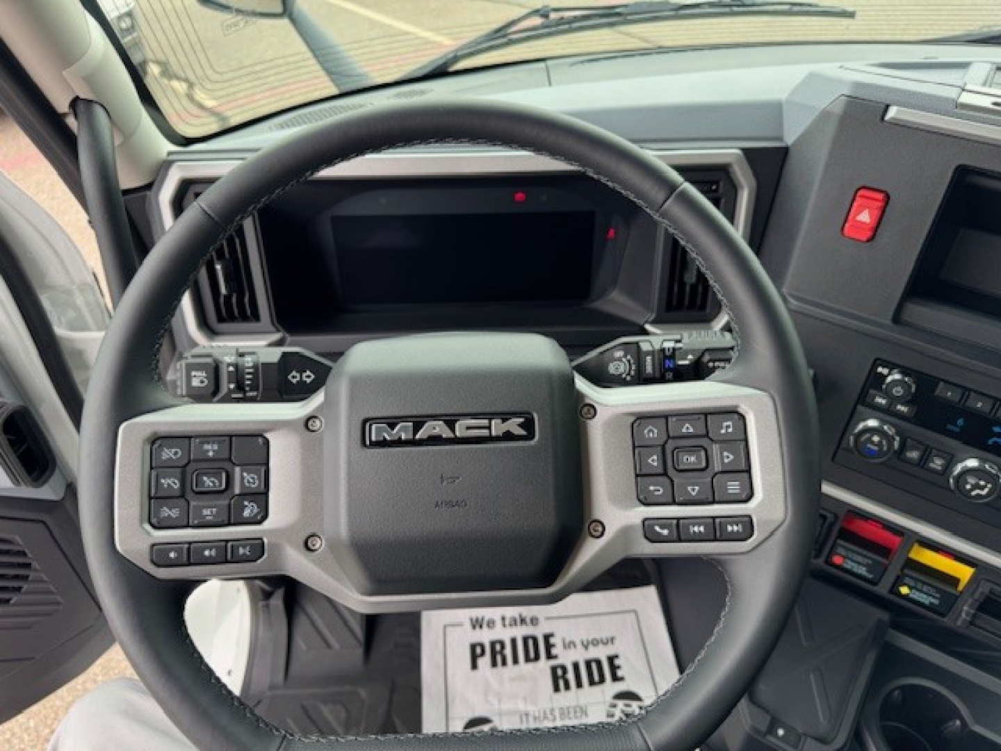Steering wheel and dashboard of a 2027 Mack AN64T conventional daycab showing center console, steering column controls, and digital gauge display.