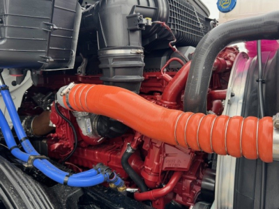 Mack AN64T engine bay with red components, orange turbo hose, blue coolant/air lines, and black air intake housing shown from front-left side.