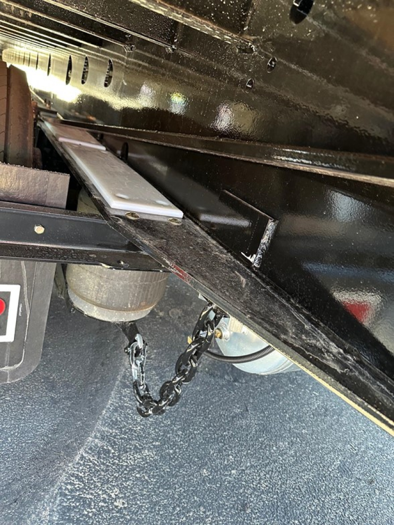 Trailer undercarriage showing chain and winch mounting, black painted steel frame, and air ride components underneath a Doepker travel trailer axle.