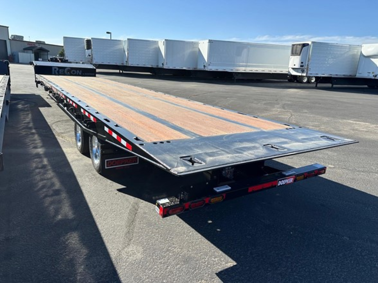 Doepker flatbed trailer rear perspective showing 40 ton slide axle, 20k winch, and wooden deck with steel ramp inlay.