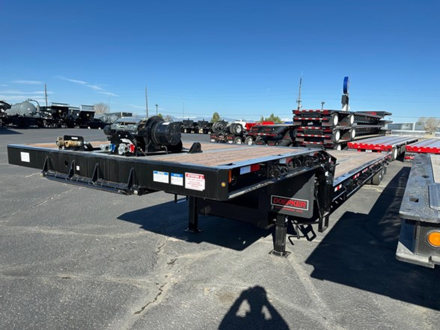Doepker 40 ton slide axle trailer with 20K winch and air ride visible in yard; multiple other trailers and components in background.