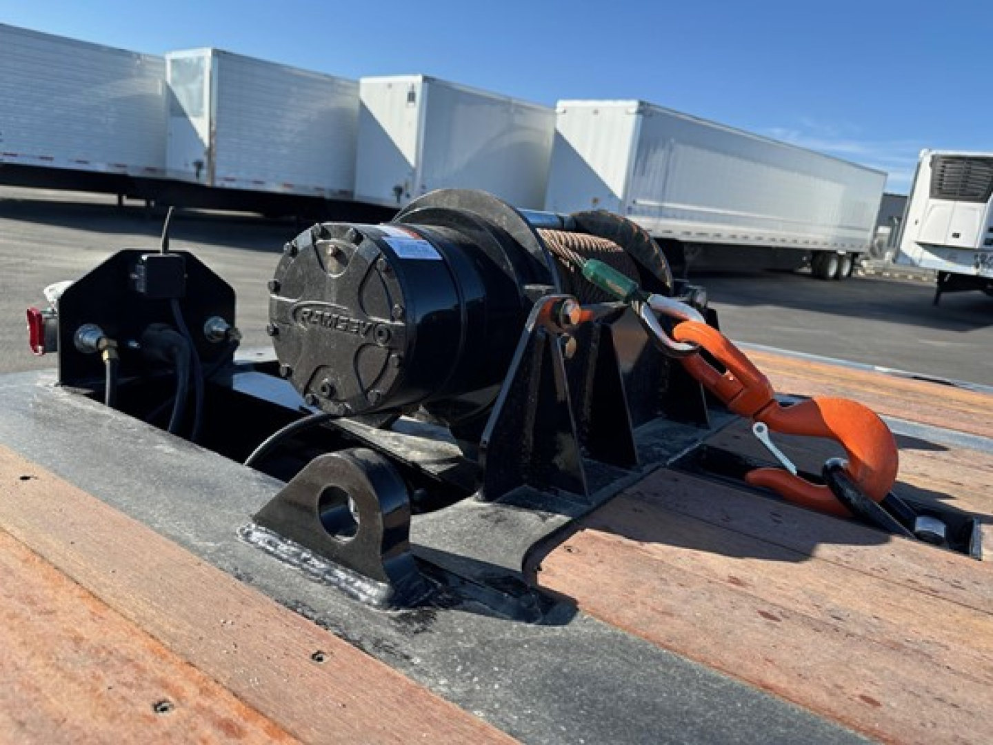 Winch and boom assembly on a Doepker 40 ton sliding axle trailer hitch, with orange tie-down strap, on a flatbed deck.