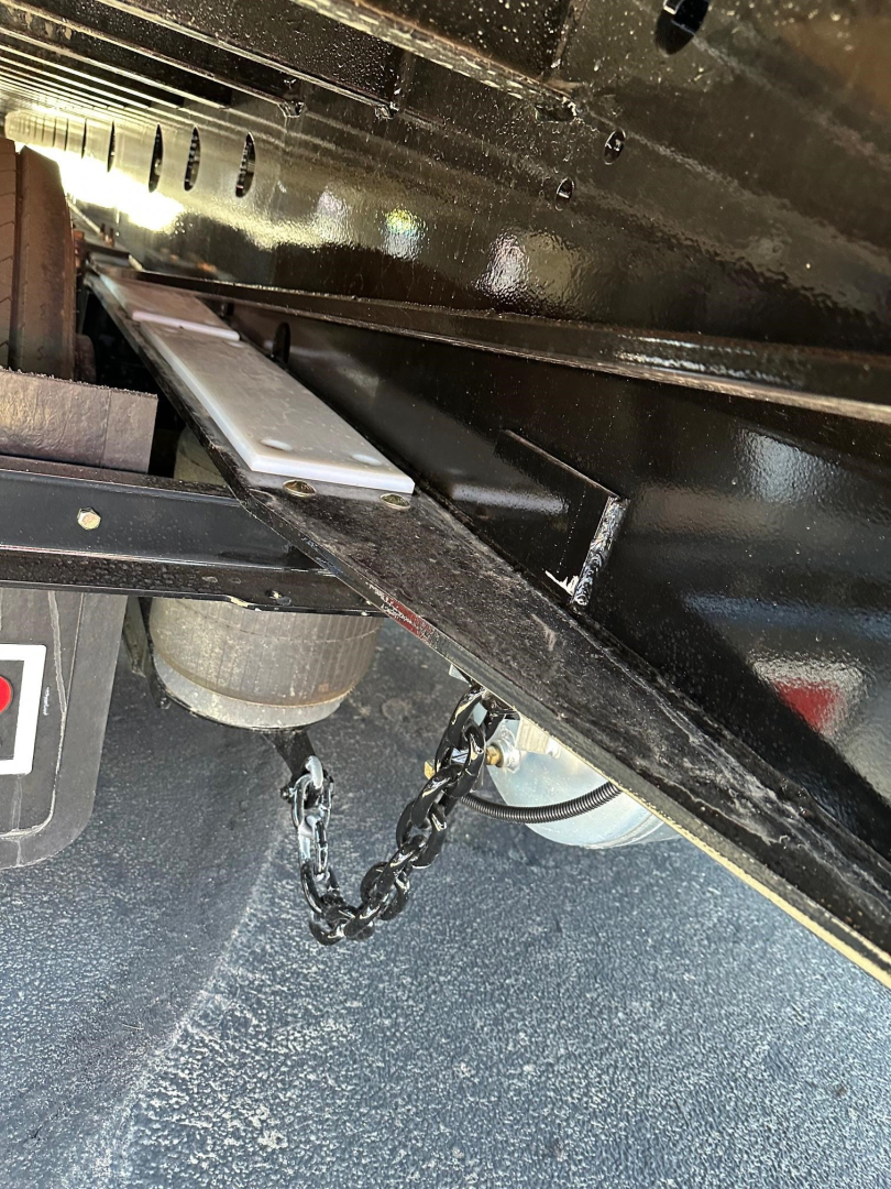 Trailer undercarriage showing metal frame and suspension components of a Doepker slide axle trailer, with chain and wheel hub visible.