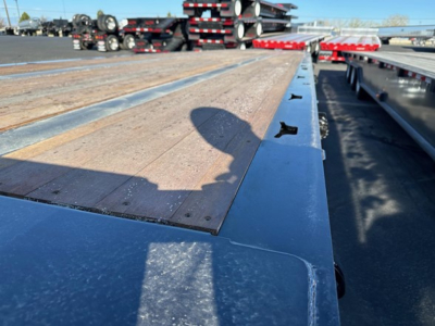 Doepker 40 ton slide axle trailer deck with wood planks and steel frames; long flatbed with winch in distance; equipment yard in background