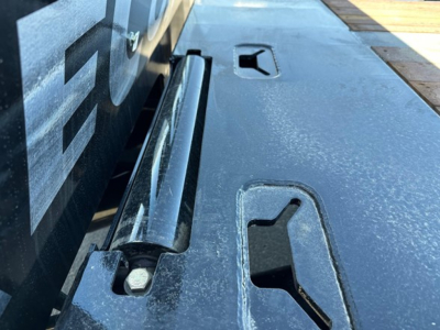Doepker trailer component close-up showing slide axle and winch mounting area, with textured steel surface and access slots.