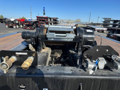 Winch assembly on a trailer frame with a hand crank and hydraulic components, 40 ton slide axle trailer winch rig, visible bolts and metal fittings.