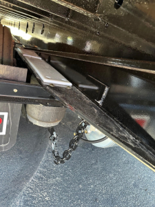 Trailer undercarriage showing metal frame and suspension components of a Doepker slide axle trailer, with chain and wheel hub visible.