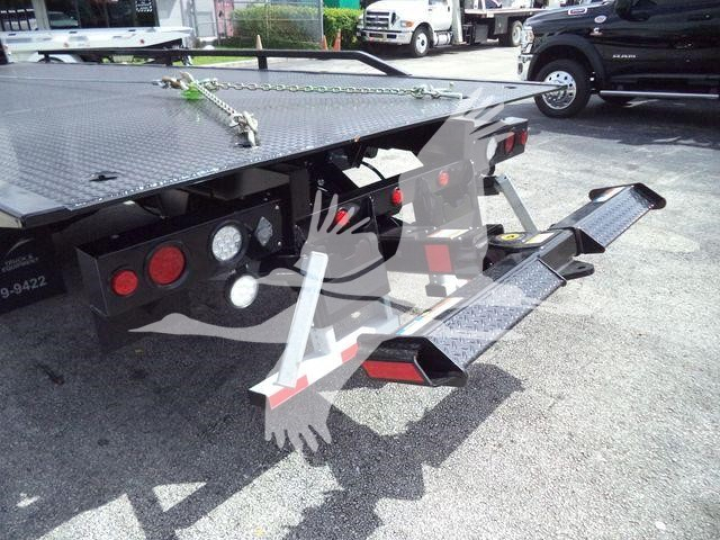 Truck flatbed with foldable ramps and rear lights showing on a rollback trailer.