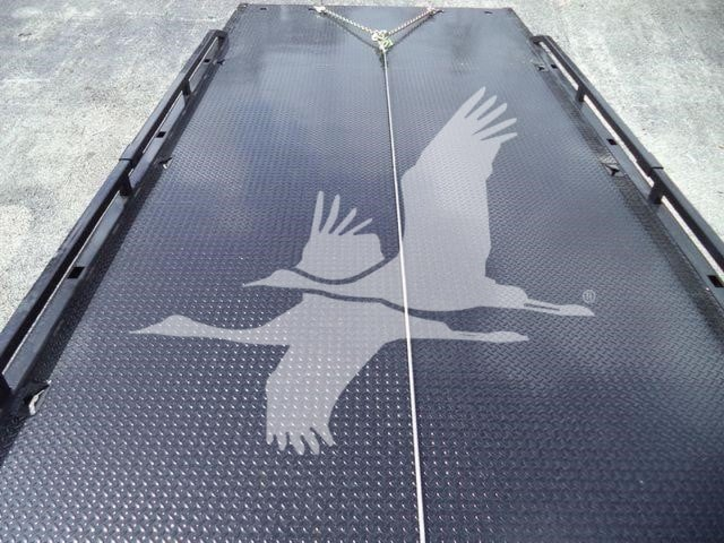 Flatbed or loading deck with two large bird logos (eagles) in a light color; tie-down straps visible at top center; black textured surface.