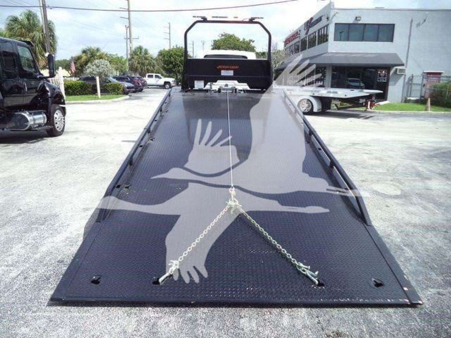 Image of a new 2027 International MV rollback truck with a flatbed, chains securing the ramp, and a black guard at the far end.