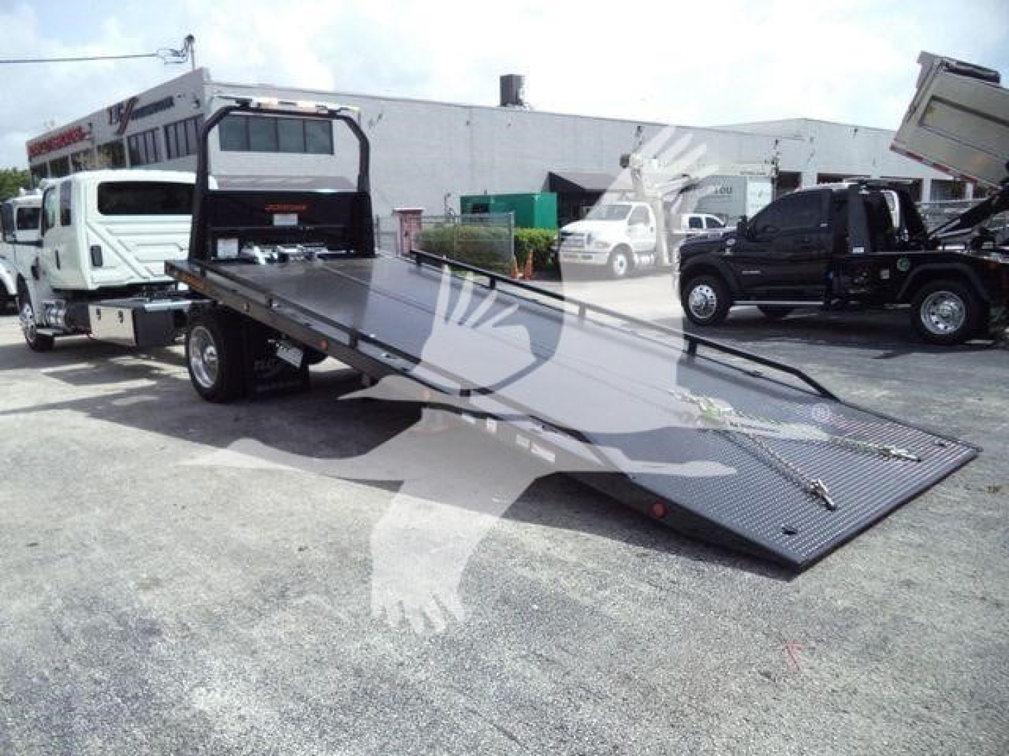 Flatbed tow truck with a long lowered ramp bed in a dealership lot, International MV captioned image.