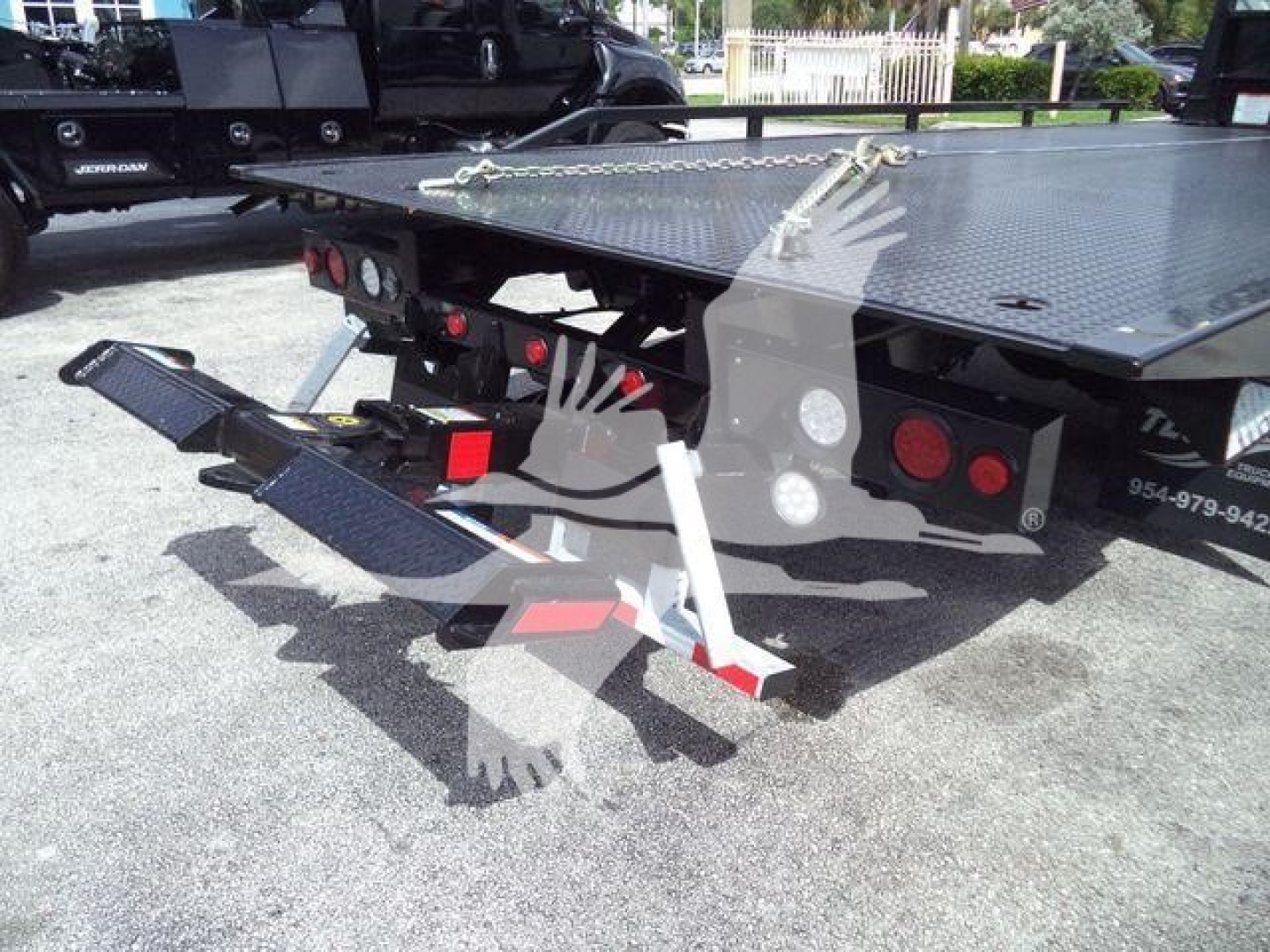 Truck rollback equipment with fold-down ramps and rear lighting, viewed from rear-left corner; platform with diamond plate surface; hydraulic stabilizer leg visible.