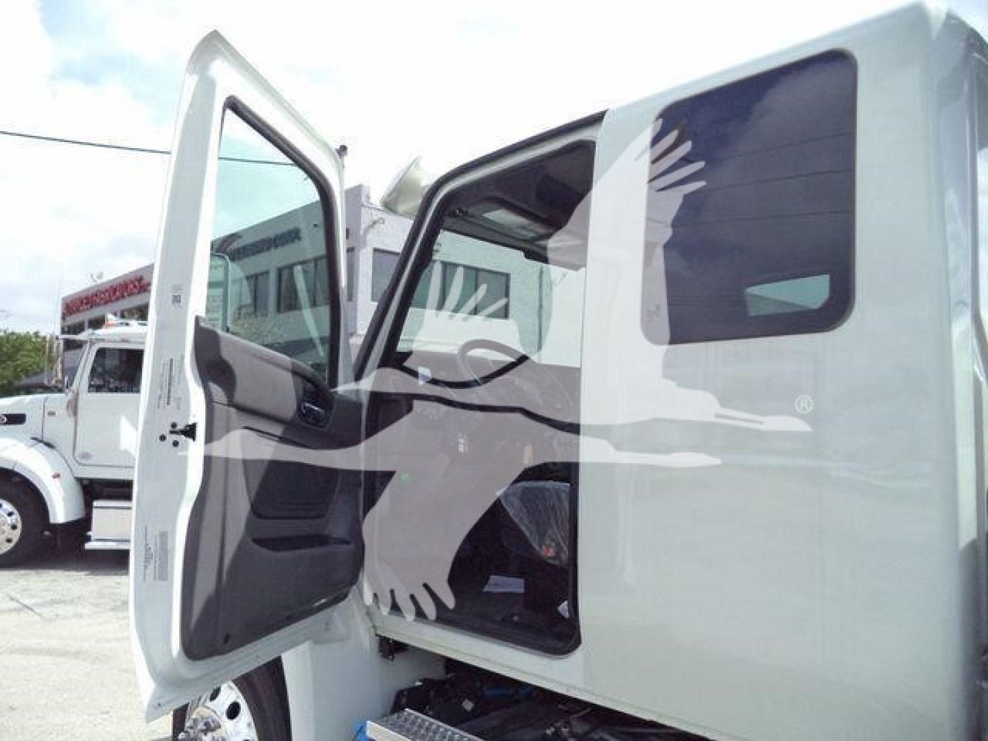 Truck cab interior visible; open door shows driver seat and steering area with side mirror. Background shows other trucks and dealership lot.