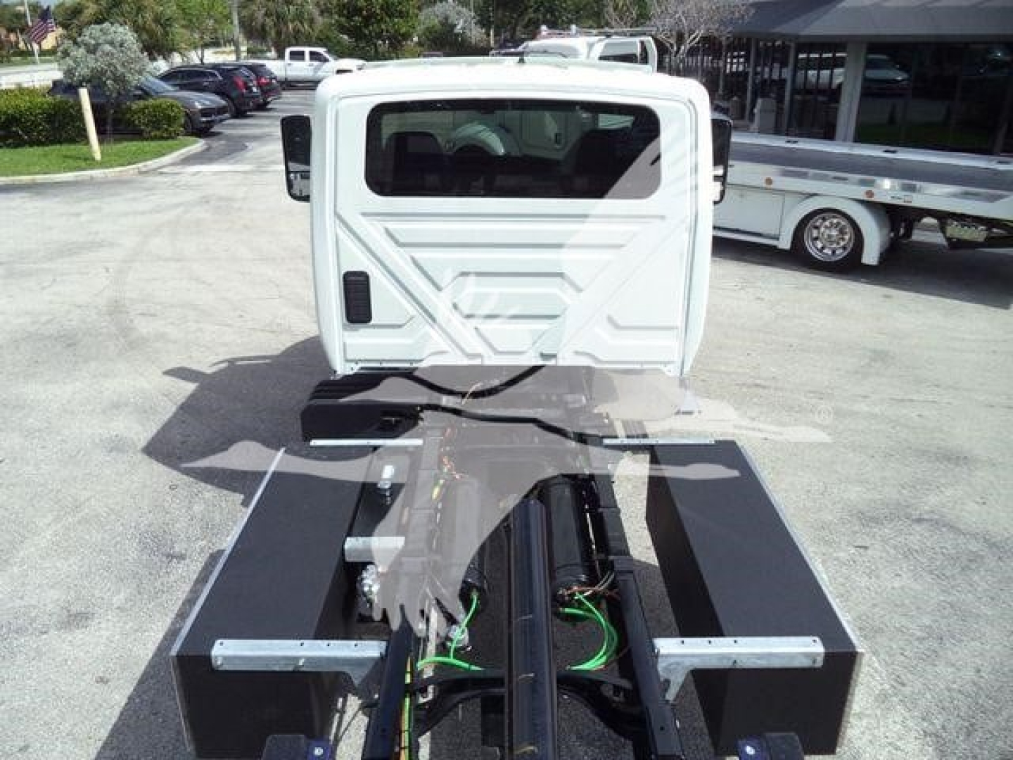 Truck cab rear view mounted on a rollback chassis with exposed frame and hydraulic lines.