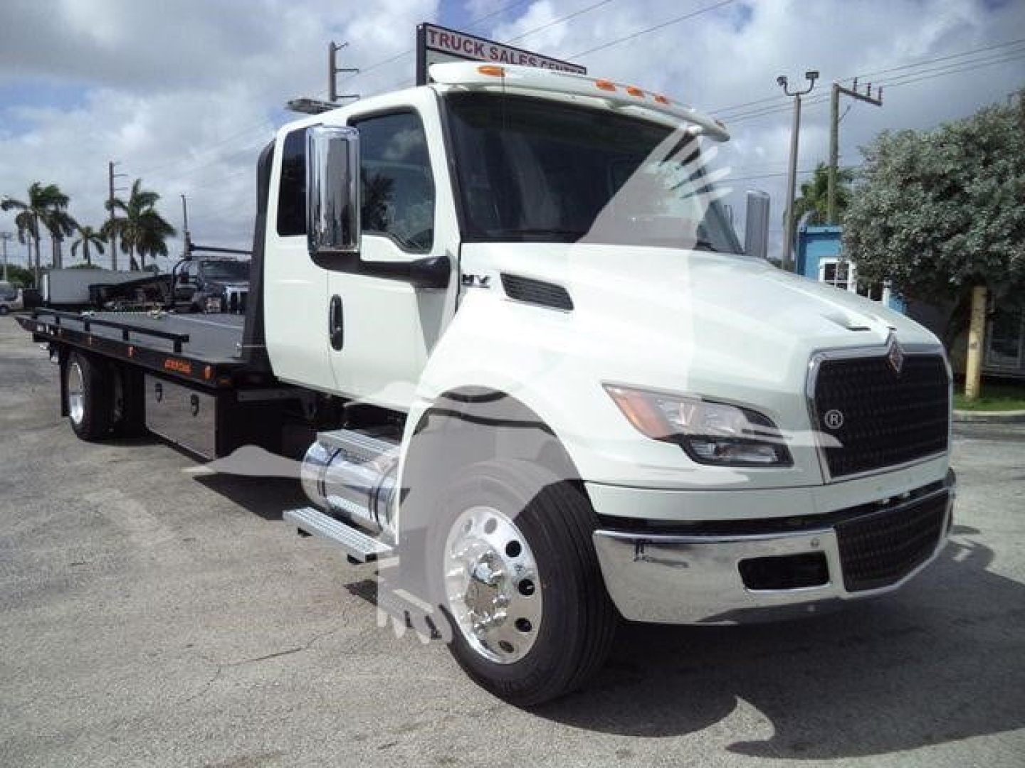 Truck with rollback bed showing International MV branding and white cab in a dealership lot.
