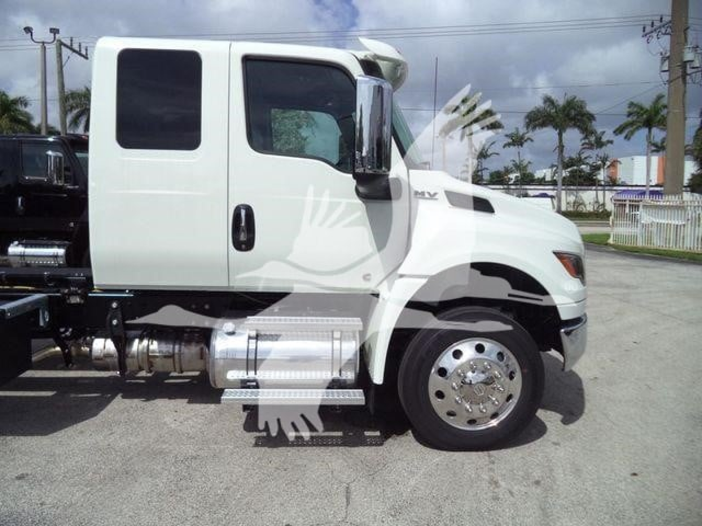 Truck engine bay side view of a white 2027 International MV rollback truck showing cab, front wheel, and chrome fuel tank.