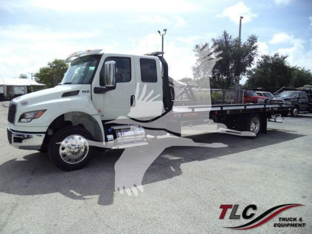 International MV rollback truck side view showing flatbed with reflective decal and chrome fuel tanks.