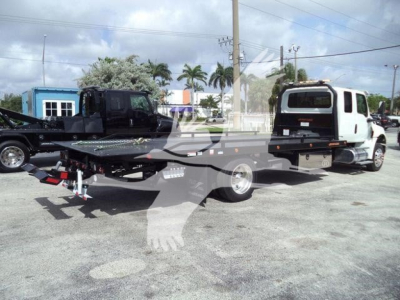 2027 International MV rollback truck showing flatbed trailer with loader in background and palm trees.