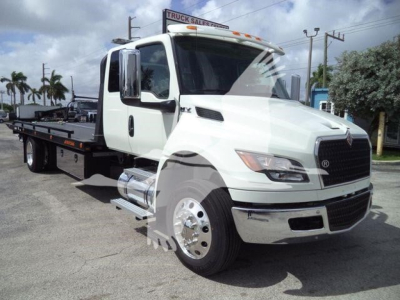 Truck with rollback bed showing International MV branding and white cab in a dealership lot.