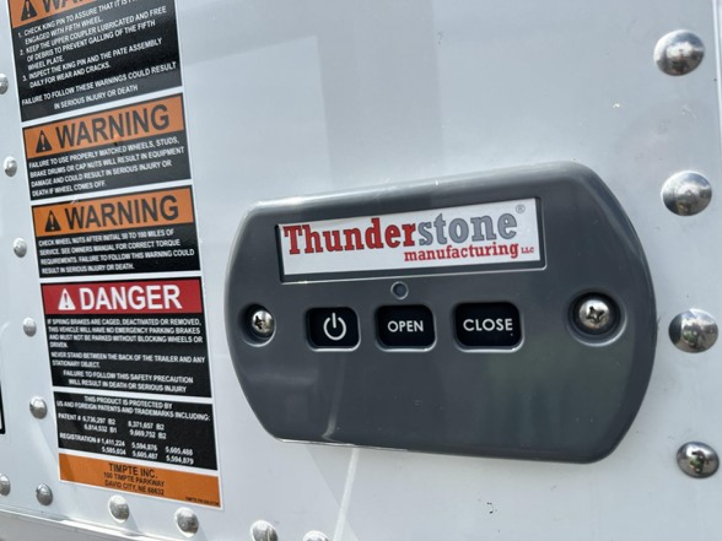 Trailer side with Thunderstone manufacturing control pad labeled OPEN/CLOSE and warning stickers on left; Thunderstone logo on pad.