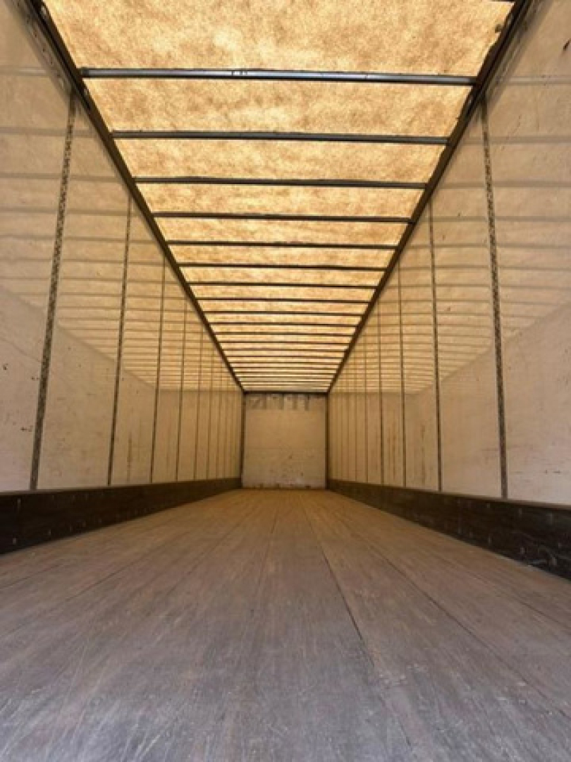 Interior of a Wabash trailer with long empty cargo area, tan walls, ribbed ceiling, and wooden floor. No visible text or labels.