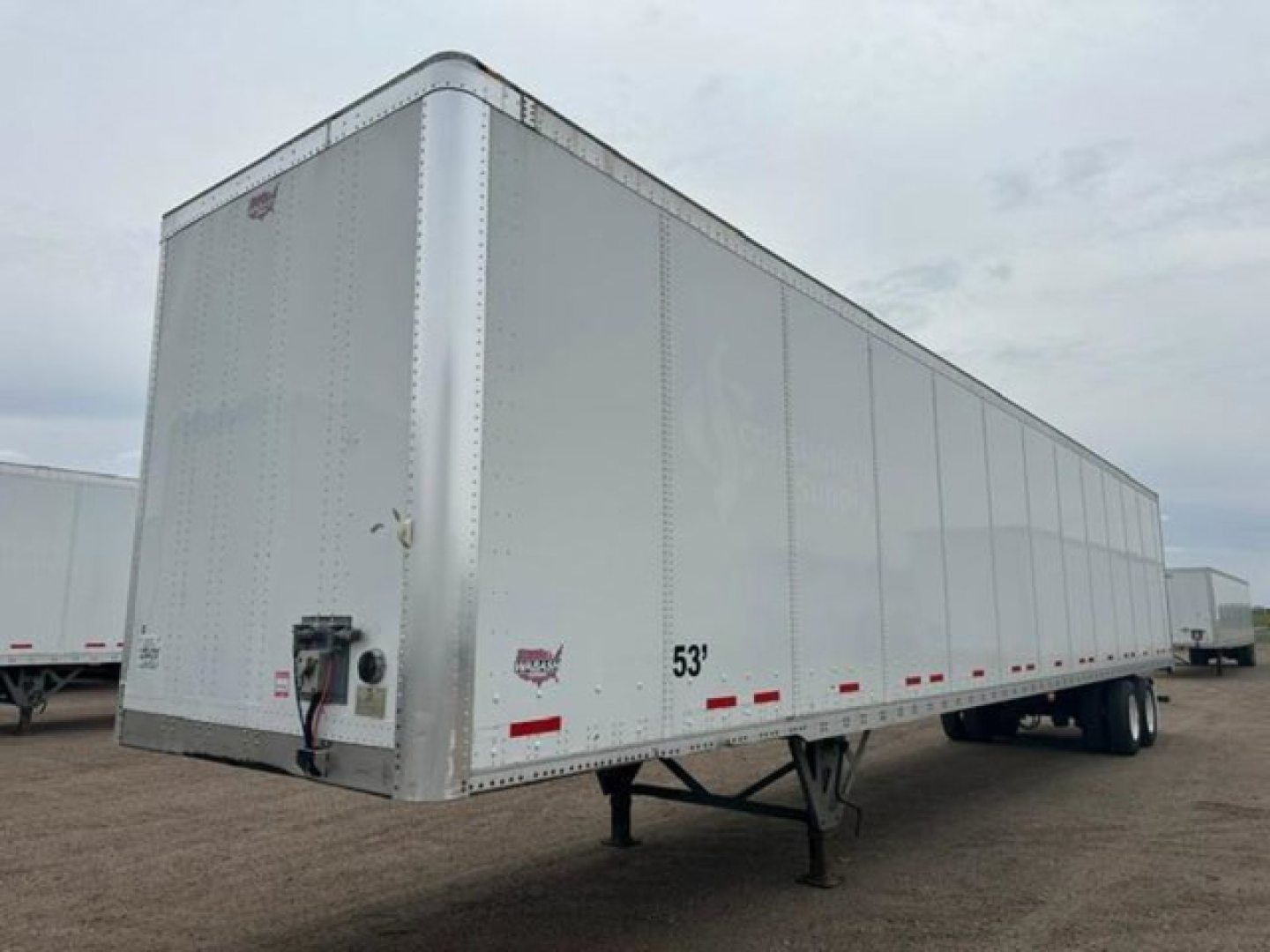 Trailer side view showing 53' length with silver aluminum body, front access panel, landing gear, and wheels visible; small decals and red reflective tape along lower edge.