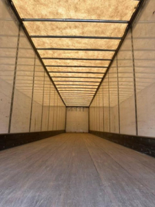 Interior of a Wabash trailer with long empty cargo area, tan walls, ribbed ceiling, and wooden floor. No visible text or labels.