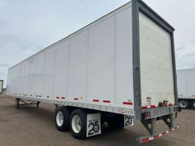 Trailer side view showing a white dry van trailer with tandem axles, riveted panels, and rear doors. Visible decals include '2 6' placards and small red/white reflective tape along the lower edge.