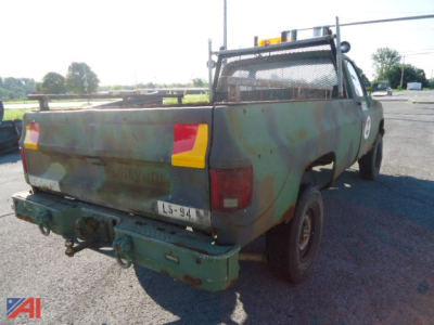 1985 Chevrolet Military D30 pickup truck rear/side view showing camouflage paint, tailgate, hitch, and mesh cab protector.