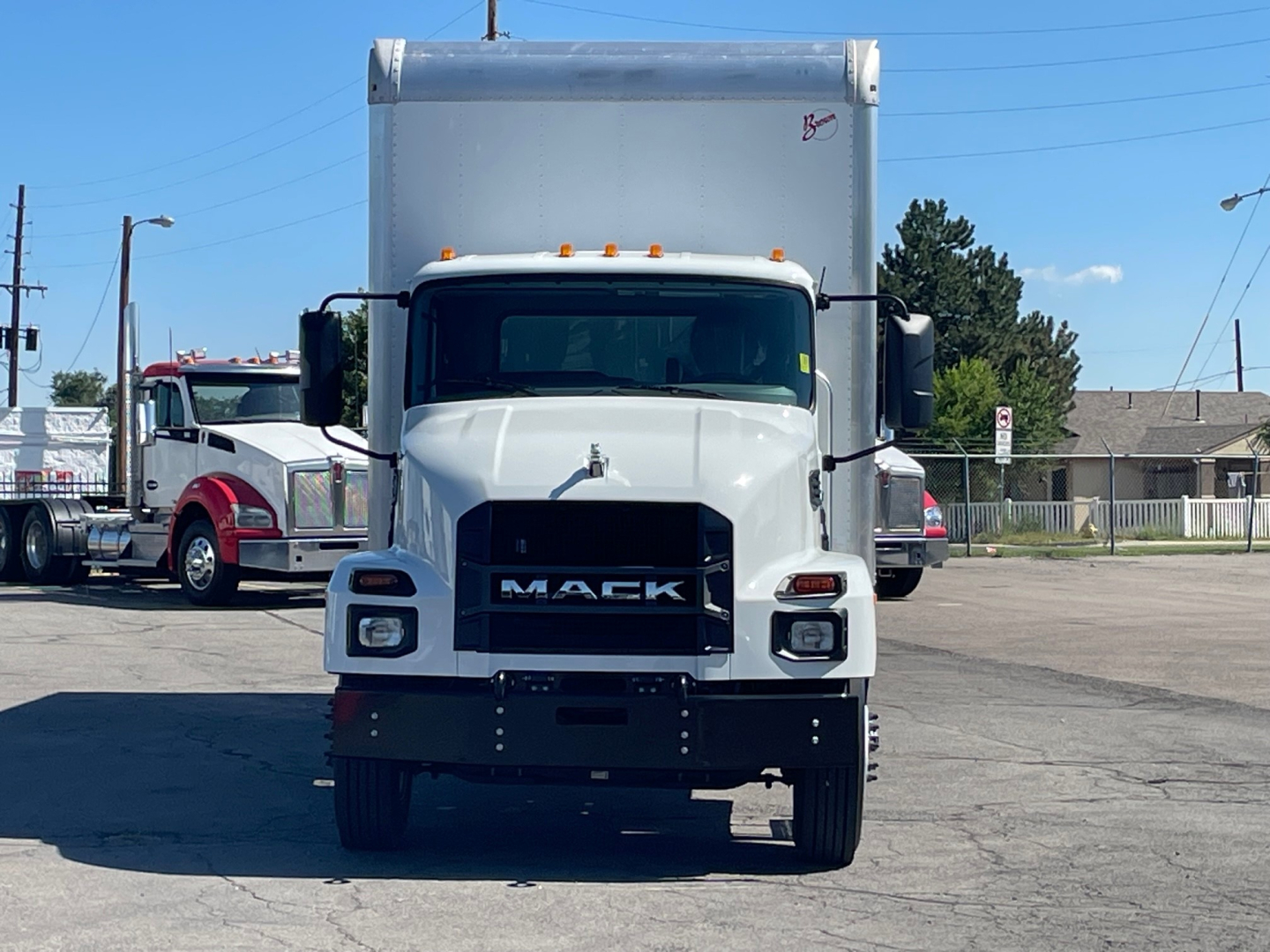 Front view of a white 2025 Mack MD6 box truck with black grille showing MAC K lettering, large bumper, and side mirrors.