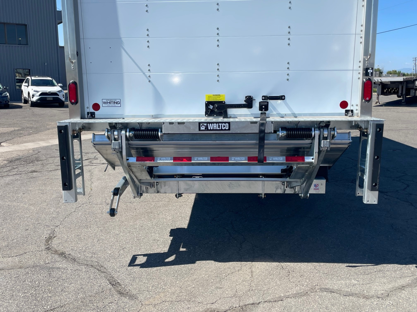 Rear view of a Mack MD6 box truck showing steel bumper with drop-down steps and reflectors; hardware and tailgate latches visible.