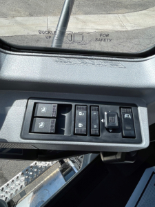 Dashboard controls and window switch panel inside a Mack MD6 cab with multiple switch buttons and a rear view mirror reflection