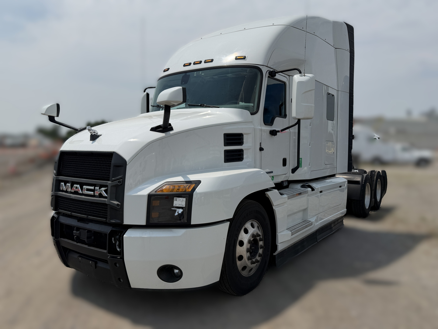 Truck: 2024 Mack AN64T70 conventional sleeper with white cab and raised sleeper, showing front grille with MACK logo and dual fuel tanks, three-axle configuration.
