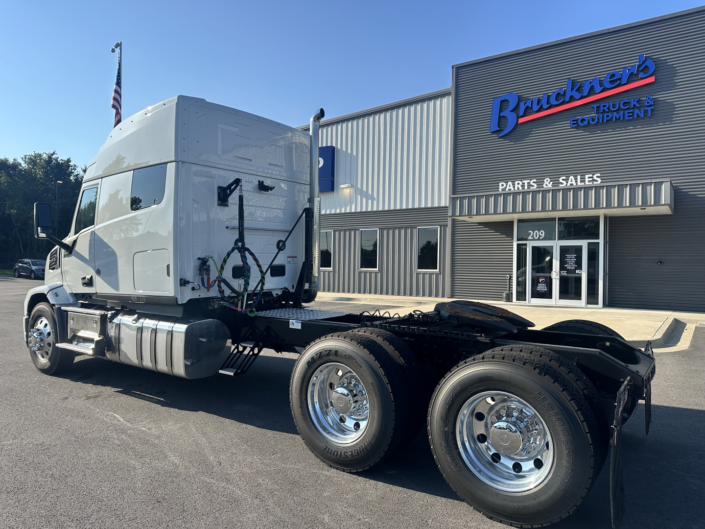 Truck chassis and cab of a new 2027 Mack PR64T76M with dual rear axles, showcased outside a parts and sales building.