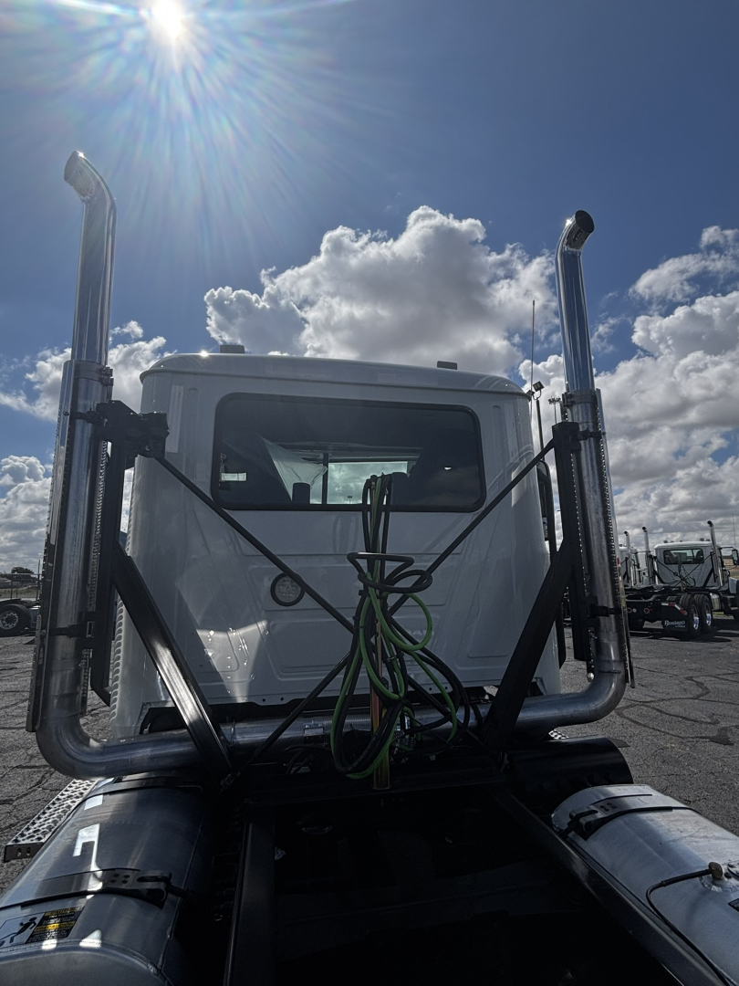 Truck cab of a 2027 Mack GR64FT in-view from behind with chrome vertical exhaust stacks and green hoses on the star-of-daycab, front window visible.